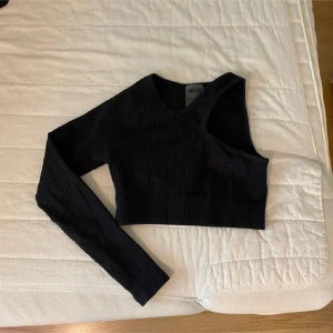 Svart oneshoulder ribbad topp - Snygg svart oneshoulder topp med ribbad struktur. Toppen är croppad och har en lång ärm, tröjan är en träningströja men går att använda till vardags också 🤍