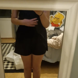 Svart korta short - Säljer en stilren svart kort short med en tight passform. Shortsen är ärmlös och perfekt för en kväll ute. Den har en enkel design som gör den lätt att matcha med olika accessoarer.