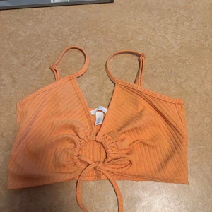 Orange ribbad linnetopp - Säljer en snygg orange ribbad linnetopp med knytning framtill. Perfekt för varma sommardagar eller en kväll ute. Toppen har smala axelband och en trendig croppad stil.