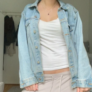 Ljusblå jeansjacka - Säljer en klassisk ljusblå jeansjacka med knappar framtill och två bröstfickor. Jackan har en rak passform och långa ärmar. Perfekt att slänga över en t-shirt eller hoodie för en avslappnad look.