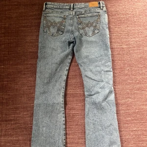 Ljusblå bootcut jeans  - Säljer ett par ljusblå jeans med klassisk bootcut-passform. Jeansen har broderade detaljer på bakfickorna och låg midja. Perfekta för dig som gillar en tidlös denimlook.