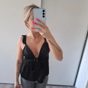 Svart omlott linnetopp med knytband - Säljer en svart omlott linnetopp med djup v-ringning och breda axelband.