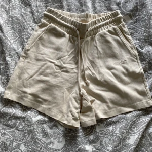Beige shorts från AWARE by Vero Moda - Snygga beige shorts från AWARE by Vero Moda med resår i midjan och dragsko. Mjukt bomullsmaterial och två sidofickor. Perfekta för varma dagar och en avslappnad stil.