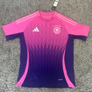 Tyskland bortaställ matchtröja 2024 - STORLEK M. Snygg Tyskland fotbollströja från Adidas i rosa och lila. Jätte bekväm och skön att ha på sig. Helt oanvänd och helt ren. Perfekt till sommaren. PRISET KAN DISKUTERAS