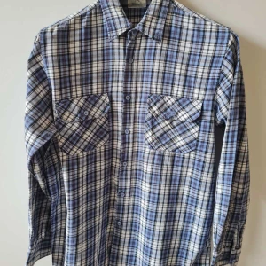 Blårutig skjorta från WORKER strl L - Snygg blårutig skjorta från WORKER med klassisk krage och två bröstfickor med knappar. Skjortan har långa ärmar och är tillverkad i 100% bomull. Bröstmått 114cm. Storlek L. Kan hämtas i Vallentuna.