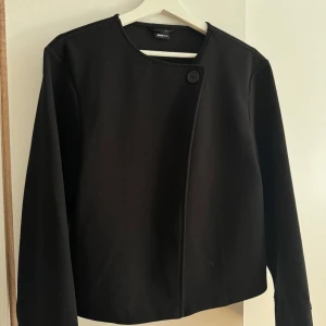 Svart kappa från Gina Tricot - Säljer en kortare kappa från Gina Tricot i storlek XS. Jackan har en minimalistisk design med rund halsringning och knäppning med en knapp upptill. Använd en gång och köpt förra året.