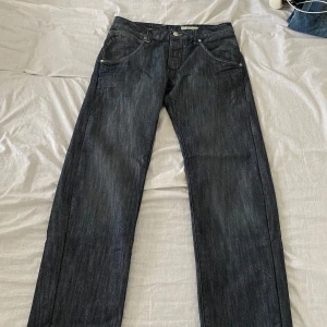 Mörkblå jeansbyxor från &Bragg - Säljer ett par mörkblå jeansbyxor från &Bragg med klassisk femficksdesign och raka ben. Byxorna har silverfärgade knappar och detaljer samt en fitted waist och straight fit. Perfekta för en stilren och enkel look.