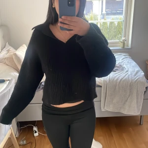 Svart croppad stickad tröja med krage - Säljer en svart croppad stickad tröja med krage och långa ärmar. Tröjan har en avslappnad passform och är perfekt för en stilren och enkel look.