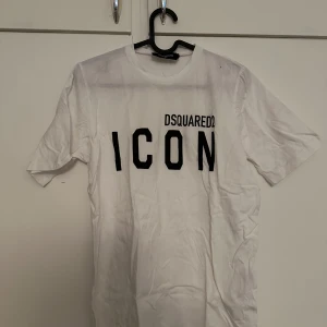 Vit t-shirt från Dsquared2 med tryck - Vit t-shirt från Dsquared2 med svart text 'ICON' och logga på bröstet. Klassisk passform och rund halsringning. Perfekt för en stilren och trendig look.