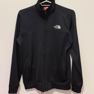 Svart jacka från The North Face - Säljer en svart jacka från The North Face med dragkedja framtill och hög krage. Jackan har två fickor med dragkedja och en diskret logga på bröstet. Perfekt för dig som gillar North Face pris :299kr