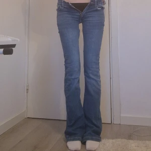 Blå bootcut jeans med detaljerade bakfickor - Säljer ett par blå bootcut jeans,  låg midja och snygga detaljer på bakfickorna. Jag har sytt om dem så att de blev till låg midja och de är bra skick. Midjamått: Ca 33cm rakt över