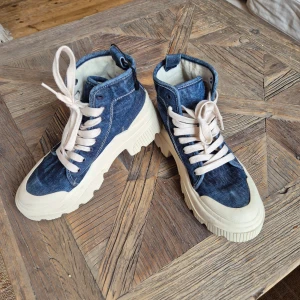 Chunky denim sneakers med vit sula - Säljer ett par chunky sneakers i blått jeanstyg med kraftig vit sula och vita snören. Skorna har högt skaft och cool streetstil, perfekta för dig som vill sticka ut. Passar till många olika outfits och ger en trendig look.