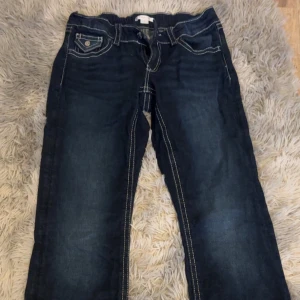 Mörkblå jeansbyxor från Gina Tricot - Säljer ett par mörkblå jeansbyxor från Gina Tricot med kontrastsömmar och klassiska fickor fram och bak. Byxorna har normal passform och ät boot cut,samt snygga detaljer med knappar på fickorna.