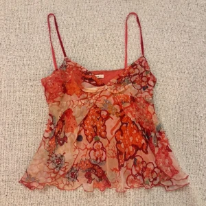 Flerfärgad topp med paljetter - Superfin linnetopp med tunna axelband från Diane von Furstenberg. Toppen har ett blommigt mönster i rött och orange med inslag av pärlor och paljetter. Materialet är lätt och genomskinligt, perfekt för varma dagar, materialet är 100% silke