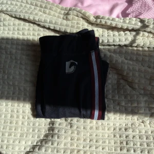 Svarta ridleggings med rödvit rand - Säljer ett par svarta ridleggings från Covalliero med röd och vit rand längs sidorna. Byxorna har perforerade detaljer längs benen för extra ventilation och är tillverkade i stretchigt material för bästa komfort💞