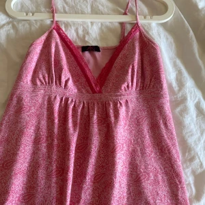 Rosa topp med spets från Ann Christine - Söt rosa topp från Ann Christine med smala axelband och v-ringning dekorerad med spets. Klänningen har ett diskret paisleymönster och är perfekt för varma dagar. Köparen står för frakt om vi inte kommer överens om annat❤️