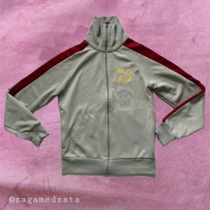 Vintage Gråbeige track jacket från Puma S - Sportig gråbeige track jacket från Puma med röda ränder längs ärmarna och gul Puma-logga på bröstet. Jackan har hög krage, hel dragkedja och ribbade muddar. Perfekt för en chill streetstyle-look.