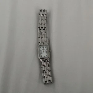 Silverfärgad rektangulär klocka från mockberg - Stilren klocka från mockberg med rektangulärt vitt ur och romerska siffror. Armbandet är i silverfärgad metall med klassisk länkdesign. Perfekt accessoar för dig som gillar en tidlös och clean look.