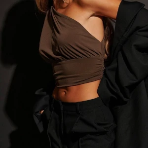 Oneshoulder croppad topp i svart  - Hanna schönberg x NAKD, säljer den i svart. Trendig croppad topp med oneshoulder-design och snygga rynkade detaljer i midjan. Toppens asymmetriska snitt ger en cool vibe och den sitter tight över kroppen.