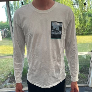 Vit långärmad Lee-tröja med print - Vit långärmad tröja från Lee i bomull med avslappnad passform. På bröstet finns ett tryck med palmmotiv och svart ram. Rund halsringning och mjukt material som känns skönt mot huden. Perfekt för dig som gillar stilrena plagg med en twist.