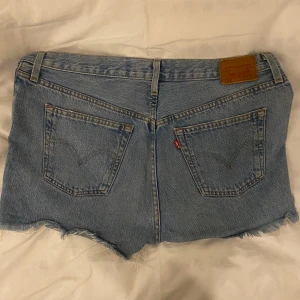 Levi's jeansshorts - Ljusblå jeansshorts från Levi's med klassisk femficksdesign, knappar framtill och hög midja.👖Shortsen har bälteshällor och den ikoniska Levi's-lappen bak. Säljer denna då dem ej kommer till användning längre. Dem har använts i ett par år och är därmed ganska använda. 😇Däremot har shortsen inga defekter som är varken synliga eller funktionella.🤩🙌🏽