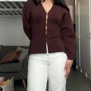 Slutsåld Vinröd blus med v-ringning och knappar - Säljer en stilren vinröd blus med v-ringning och dekorativa knappar framtill. Blusen har lång ärm och en figurnära passform som ger en snygg siluett. Perfekt för dig som gillar minimalistisk och trendig stil.