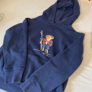 Mörkblå Polo Bear hoodie från Ralph Lauren - Mörkblå hoodie från Ralph Lauren med ikoniska Polo Bear-trycket framtill. 