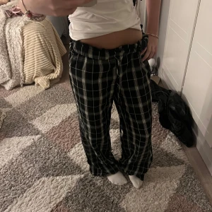 Svarta rutiga mjukisbyxor med snörning - Säljer ett par svarta mjukisbyxor med vitt rutmönster och snörning i midjan. Byxorna har loose fit och resår i midjan för extra komfort. Perfekta för chill dagar hemma eller när du vill vara bekväm men ändå se snygg ut.