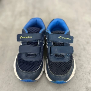 Blå sneakers från Energetics med kardborre - Mörkblå sneakers från Energetics med vit sula och blå detaljer. Ovandelen är i mesh och syntet för bra andningsförmåga. Skorna har två praktiska kardborreband och en sportig look med vita detaljer på sidorna. Perfekta för dig som gillar en aktiv stil. 