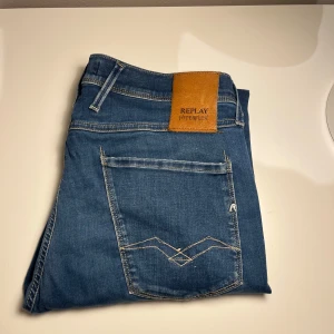 Blå jeans från Replay - REPLAY ANDBASS!Snygga blå jeans från Replay Hyperflex med klassisk femficksdesign och knappgylf. De har en stilren look med diskreta sömmar och en läderpatch med logga på baksidan. Perfekta för en avslappnad stil.Storlek 32. Nypris 1700kr. Vårt pris 280kr🤩