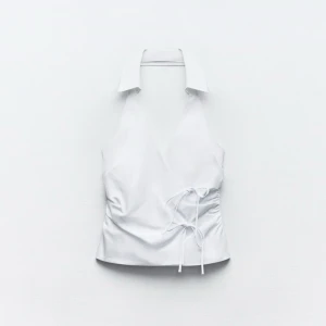 Vit omlott halterneck topp XS - Säljer en vit halterneck topp från Zara i omlottmodell med krage och snörning i sidan. Toppen är ärmlös och har öppen rygg, perfekt för en trendig och fräsch look. Materialet är bomull och toppen har en snygg v-ringning framtill.