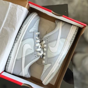 Nike Dunk Low Pure Platinum 36.5 - NYSKICK!! Använt 2-3ggr,  skickas i original förpackning. Fick i present och kommer därför donera intäkterna från försäljning.                                                ‼️Helt nya i box brukar gå för ca 1200–2000 kr.                                             ➡️Nike Dunk Low sneakers i färgen Pure Platinum/White-Wolf Grey. Skorna har en clean och stilren look med ljusgrå och vita paneler i skinn, klassisk Nike swoosh och perforerad tå. Lågt skaft och platt sula.