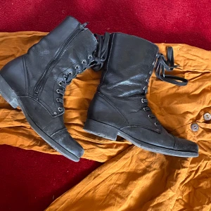 Svarta kängor från XIT stl 38 - svarta kängor i skinn med snörning framtill och dragkedja på sidan. rund tå och låg klack. väldigt mjuka o sköna att ha på sig
