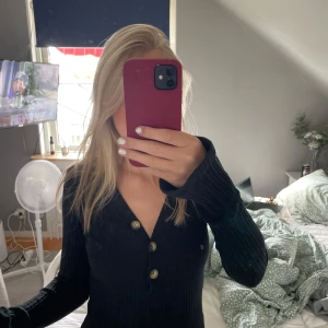 En svart ribbad klänning från Gina Tricot.  - Svart ribbad klänning från Gina Tricot med v-ringning och tre dekorativa knappar framtill. Klänningen är figurnära, har lång och utsvängd arm och är i mjukt stickat material. Perfekt för dig som gillar en enkel men snygg look 💞