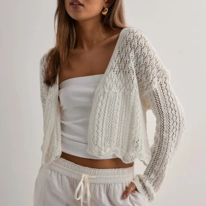 Vit stickad kofta från ONLY - Superfin vit stickad kofta från ONLY med öppen front och lång ärm. Koftan är croppad och har ett luftigt, virkat mönster som ger en chill och trendig vibe. Perfekt att slänga över ett linne eller klänning för en snygg layering-effekt.