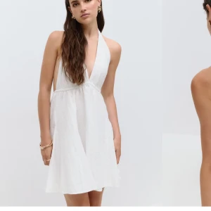 Vit kort sommarklänning med v-ringning - Superfin vit kort klänning med djup v-ringning och halterneck. Klänningen är ärmlös och har ett lätt, luftigt tyg med broderade detaljer. Perfekt för varma dagar och ger en fräsch och stilren look. Helt ny med prislapp kvar, nypris 499kr.