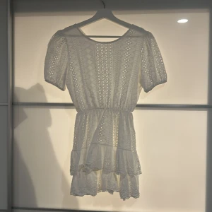 Vit spetsklänning från Lucilia - Superfin vit kortklänning från Lucilia med broderade spetsdetaljer och volang i kjolen. Klänningen har korta puffärmar, markerad midja och v-ringning i ryggen med en knap. Perfekt för sommarens! Kläningen är totalt 76 cm från axlarna och ner (bortsett från markerade midja) ! Kläning går ej att köpa eller hitta annars💗☀️