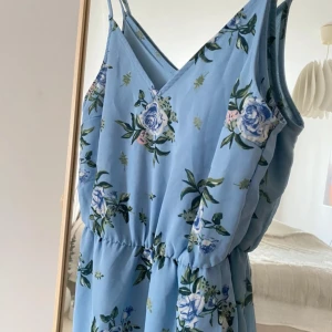 Blommig blå maxiklänning från Divided - Supersöt långklänning i ljusblått från Divided med blommigt mönster i blått, grönt och lite rosa. Klänningen har smala axelband, v-ringning och markerad midja. Perfekt för sommarens alla tillfällen!