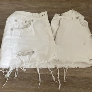 Vit jeanskjol med slitna detaljer - Vit kort jeanskjol med råa, fransiga kanter och slitna detaljer framtill. Kjolen har klassiska jeansfickor både fram och bak samt dragkedjan. Perfekt för sommaren!