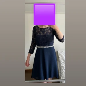 Marinblå spetsklänning med pärlmidja - Superfin marinblå klänning med blommig spets upptill och trekvartsärm. Kjolen är enkel och släpper fint från midjan som är dekorerad med pärlor. 