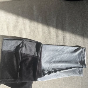 Svarta och grå leggings från H&M Sport - Snygga sportleggings från H&M Sport i svart, grått och ljusgrått. De har en tight passform och är gjorda i ett stretchigt syntetmaterial som passar perfekt för träning. Midjan är normal och designen är färgblockad för en modern look.