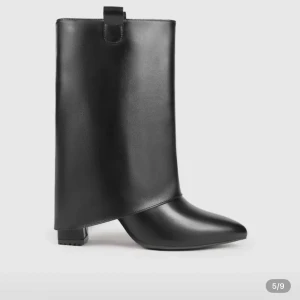 Svarta boots med spetsig tå - Unika svarta boots i skinnimitation med hög, asymmetrisk skaftdesign och spetsig tå. Snygg detalj med breda dragflikar upptill och låg klack. Perfekta för dig som vill sticka ut med en edgy och modern look.