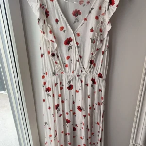 Vit blommig långklänning KappAhl XS - Supersöt långklänning från KappAhl i vitt med röda och rosa blommor. Djup v-ringning, volangdetaljer vid axlarna och lätt rynkad midja. Perfekt för sommarens alla tillfällen. Luftigt material och romantisk vibe.