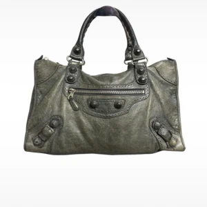 Balenciaga grå/grön skinnväska med detaljer - Cool handväska från Balenciaga i grått skinn med snygga nitar, spännen och dragkedja framtill. Väskan har dubbla handtag och en mjuk, slouchy form som ger en avslappnad vibe. Perfekt för dig som gillar statement-accessoarer med edge.