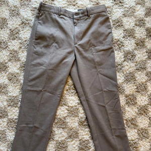 Beige kostymbyxor från H&M, regular fit - Kostymbyxor från H&M med rak passform, bälteshällor, två bakfickor med lock och knappar samt klassisk stängning fram. Har ett litet märke på höger knä.