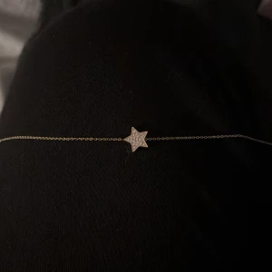 Guldfärgat armband med stjärna - Superfint armband med tunn guldfärgad kedja och en stjärnformad berlock i mitten. Stjärnan är dekorerad med små glittrande stenar som ger en extra touch. Perfekt för dig som gillar stilrena och söta smycken.