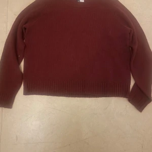 Mörkröd stickad tröja från H&M Divided - En enkel och snygg mörkröd stickad tröja från H&M Divided. Tröjan har rund hals, långa ärmar och ribbade muddar vid ärmslut och nederkant. Perfekt för lager-på-lager och passar till både jeans och kjol.