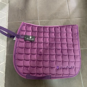 Lila schabrak!💜 - Säljer ett helt nytt schabrak från fairfield, prislapp finns kvar och aldrig använt! Ny pris 400 säljer för 200, pris kan diskuteras! Dressyr schabrak i storlek ponny! Hör av er vid frågor🥰