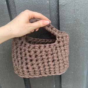 Handgjord brun virkad handväska - Unik handväska i chunky virkat material, perfekt för dig som gillar en personlig stil. Väskan är brun och har ett mjukt, grovt virkat mönster med ett litet handtag upptill. Perfekt storlek för det viktigaste.