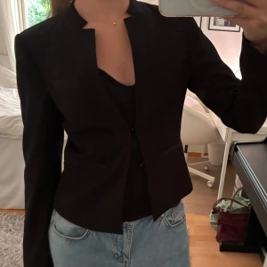 Svart blazer med knäppning  - Supersnygg svart blazer med knäppning framtill. Den understa haken är sönder (se sista bilden), men inget som påverkar helhetsintrycket! Går även att ha oknäppt